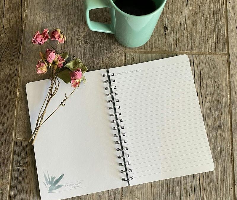 open lined journal with a green coffee mug and  a spray of pink flowers