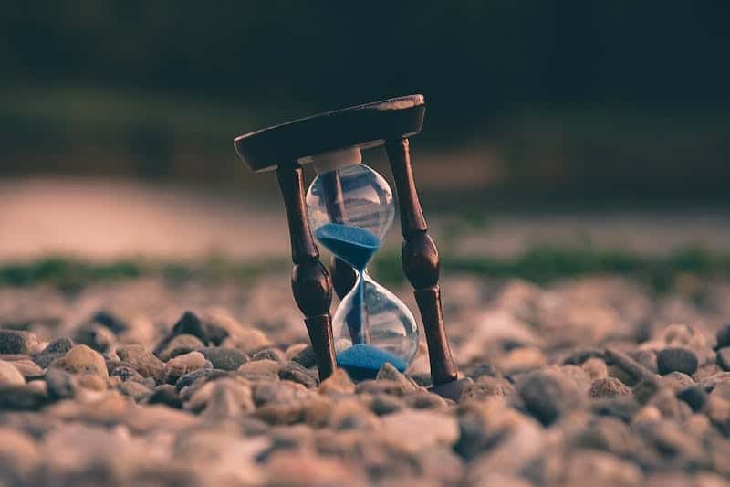 hourglass with blue sand sitting on a pebbled pathway